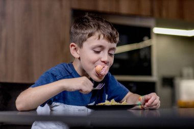 Küçük çocuk mutlu mesut sosisli makarna yiyor..