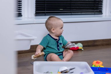 Genç bir bebek, temiz beyaz bir çöp kutusunda saklanan renkli oyuncaklarla mutlu bir şekilde oynuyor. Keşif ve etkileşimlerinden keyif alıyor.