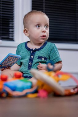 Küçük bir bebek rengarenk bir oyuncak telefonla oynarken yerde mutlu bir şekilde oturuyor ve oyun zamanının tadını çıkarıyor.