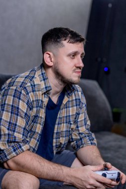 Bir adam elinde bir video oyun kumandası tutarken koltukta rahatça oturur ve oynadığı oyuna dalmıştır.