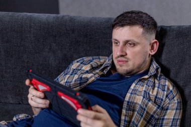 Bir adam, etrafındaki dijital dünyaya kendini tamamen kaptırmış büyüleyici bir video oyunuyla uğraşırken rahat bir şekilde kanepede uzanıyor.