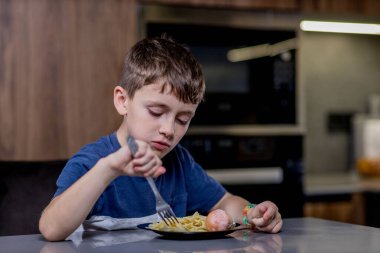 Küçük çocuk mutlu mesut sosisli makarna yiyor..