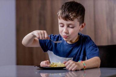 Küçük çocuk mutlu mesut sosisli makarna yiyor..