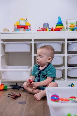 Genç bir bebek, temiz beyaz bir çöp kutusunda saklanan renkli oyuncaklarla mutlu bir şekilde oynuyor. Keşif ve etkileşimlerinden keyif alıyor.