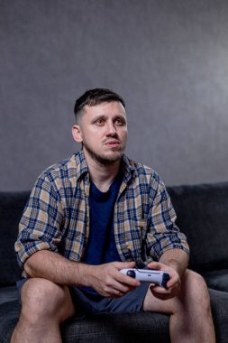 Bir adam elinde bir video oyun kumandası tutarken koltukta rahatça oturur ve oynadığı oyuna dalmıştır.