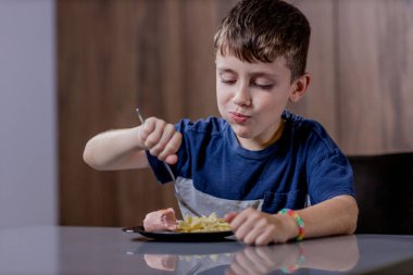 Küçük çocuk mutlu mesut sosisli makarna yiyor..