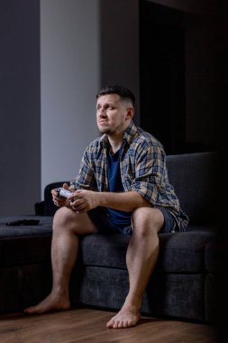 Bir adam elinde bir video oyun kumandası tutarken koltukta rahatça oturur ve oynadığı oyuna dalmıştır.