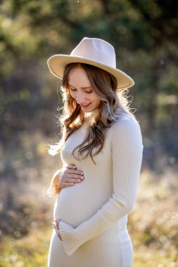 Güzel, hamile bir kadın yemyeşil bir ortamda zarifçe poz veriyor. Muazzam bir neşe ve sükunet yayıyor..