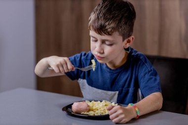 Küçük çocuk mutlu mesut sosisli makarna yiyor..