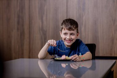 Küçük çocuk mutlu mesut sosisli makarna yiyor..