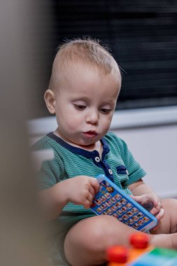 Küçük bir bebek rengarenk bir oyuncak telefonla oynarken yerde mutlu bir şekilde oturuyor ve oyun zamanının tadını çıkarıyor.