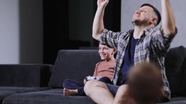 Baba ve küçük oğlu oturma odasında kanepede oturup evde video oyunları oynuyorlar..