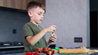 Odaklanmış bir çocuk, sıcak ve yaratıcı bir mutfakta eğlenceli kesiciler ve yumuşak hamur ile renkli kurabiyeler pişirir.