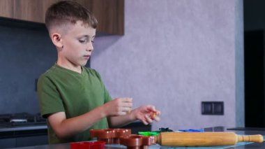 Odaklanmış bir çocuk, sıcak ve yaratıcı bir mutfakta eğlenceli kesiciler ve yumuşak hamur ile renkli kurabiyeler pişirir..