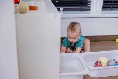 Küçük bir bebek rengarenk bir oyuncak telefonla oynarken yerde mutlu bir şekilde oturuyor ve oyun zamanının tadını çıkarıyor.