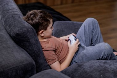 Oğlan evdeki kanepede oturup oyun oynuyor.