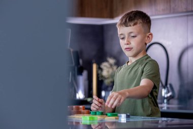 Odaklanmış bir çocuk, sıcak ve yaratıcı bir mutfakta eğlenceli kesiciler ve yumuşak hamur ile renkli kurabiyeler pişirir..