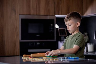 Odaklanmış bir çocuk, sıcak ve yaratıcı bir mutfakta eğlenceli kesiciler ve yumuşak hamur ile renkli kurabiyeler pişirir..