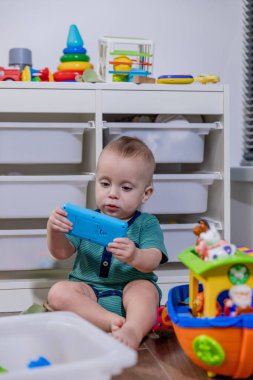 Küçük bir bebek rengarenk bir oyuncak telefonla oynarken yerde mutlu bir şekilde oturuyor ve oyun zamanının tadını çıkarıyor.