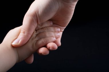 Yetişkin ve çocuk siyah arka planda el ele tutuşur