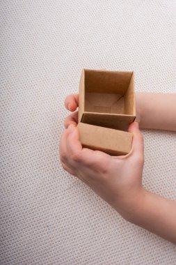 Beyaz arka planda kahverengi bir karton kutu tutuyor.