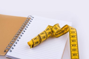 Beyaz zemin üzerinde bir not defteri yakınındaki ölçüm bandı