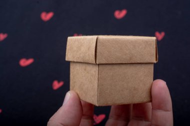 Elle tutulan karton kutu siyah arka planda kırmızı kalplerle