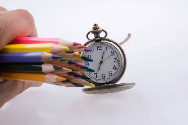 Beyaz zemin üzerinde bir cep saati yanında renkli kalemler tutan el