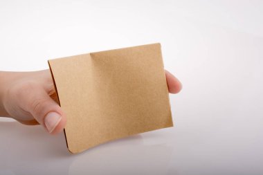 Beyaz arka planda kahverengi bir kağıt parçası tutuyor.