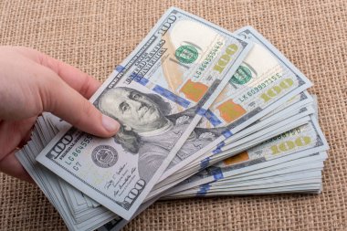 El ele tutuşan bir tomar Amerikan doları keten bir arka planda.