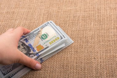 El ele tutuşan bir tomar Amerikan doları keten bir arka planda.