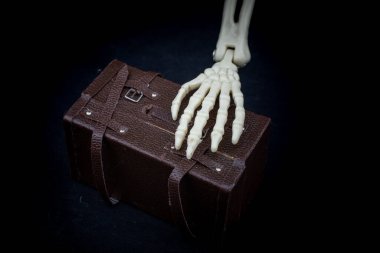 Human skeleton hand model holding a model suitcase