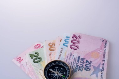 Turkish Lira banknotes by the side of a compass on white background clipart