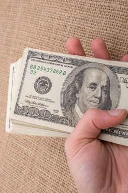 El ele tutuşan bir tomar Amerikan doları keten bir arka planda.