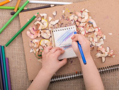 Elinde kalem çöpü olan sarmal defterlerin üzerinde renkli bir kalem tutuyordu.