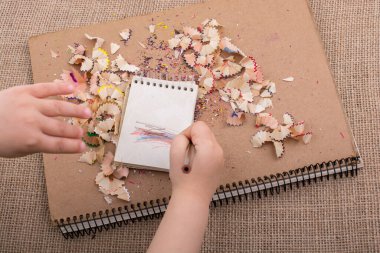 Elinde kalem çöpü olan sarmal defterlerin üzerinde renkli bir kalem tutuyordu.