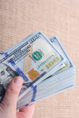 El ele tutuşan bir tomar Amerikan doları keten bir arka planda.