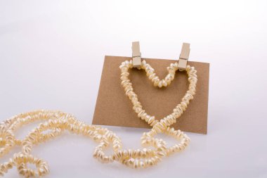 Pearl necklace forms heart shape on paper on white background clipart