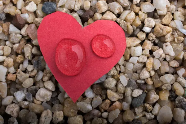 stock image Water drops on a heart shaped paper on  sand background