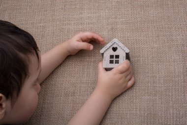 Çocuk keten bir tuvalde model bir evi tutuyor.