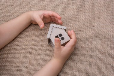 Çocuk keten bir tuvalde model bir evi tutuyor.