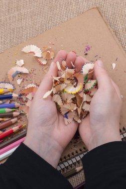 Elindeki renkli kalem talaşları bir deftere.