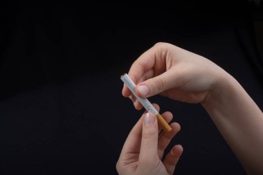 El siyah arka planda bir sigara tutuyor.