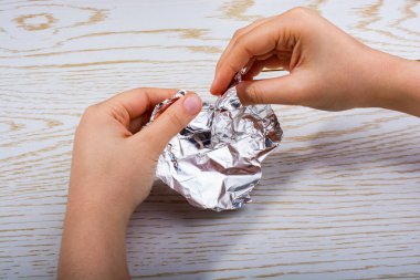 Tahta bir arka planda kalp şeklinde alüminyum folyo yırtılıyor.