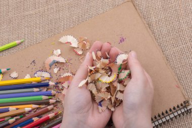 Elindeki renkli kalem talaşları bir deftere.