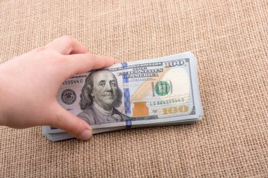 El ele tutuşan bir tomar Amerikan doları keten bir arka planda.