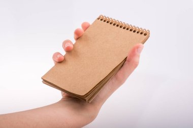 Beyaz arka planda kahverengi spiral bir defter tutuyor.