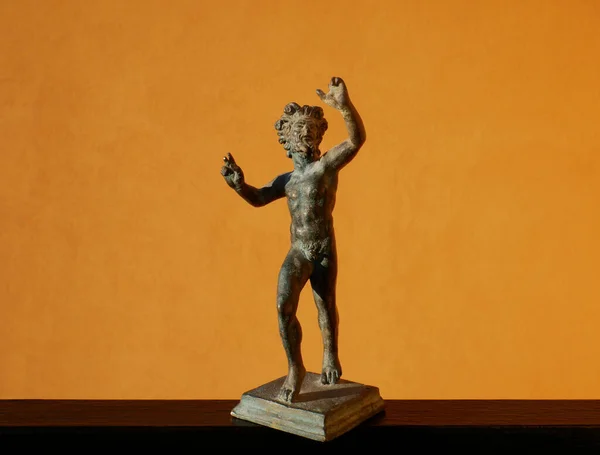 Scale reproduction on an orange background of the Roman bronze statuette of the Dancing Faun of Pompeii, National Archaeological Museum, Naples, Italy