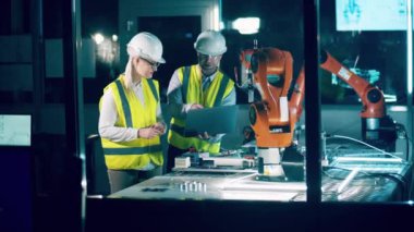 Two engineers in hardhats are talking in the robotics laboratory. 4K
