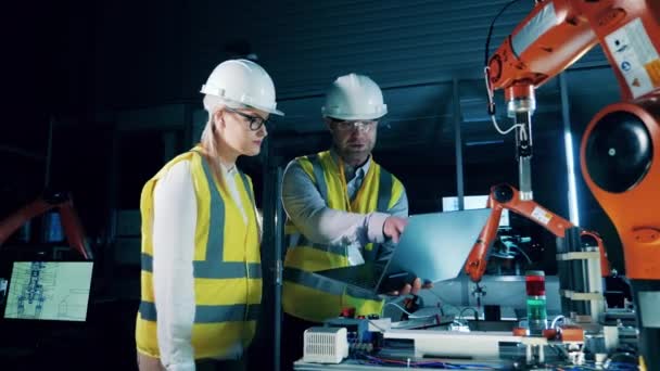 Два Инженера Касках Обсуждают Роботизированную Руку — стоковое видео